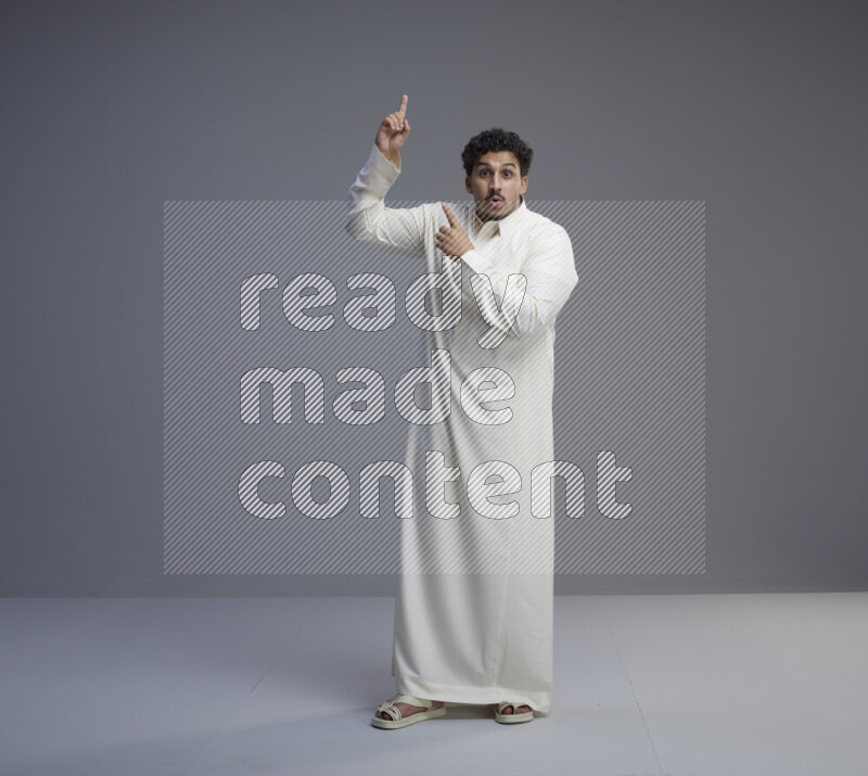 A Saudi man standing wearing thob interacting with the camera on gray background