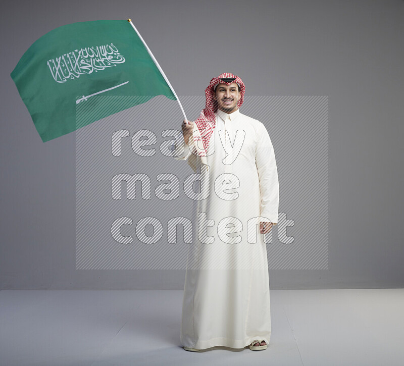 رجل سعودي يرتدي ثوب ابيض وشماغ احمر يحمل علم السعودية