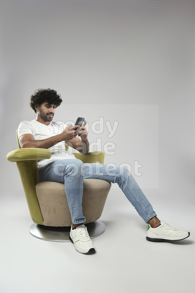 A man wearing casual sitting on a chair texting on the phone on white background