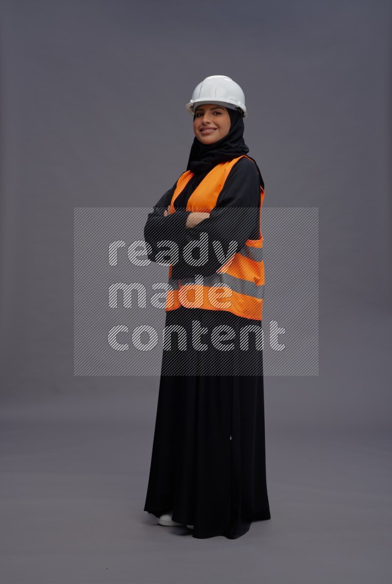 Saudi woman wearing Abaya with engineer vest standing with crossed arms on gray background