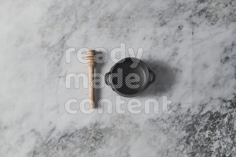 Black pottery bowl with wooden honey dipper on the side on grey marble background