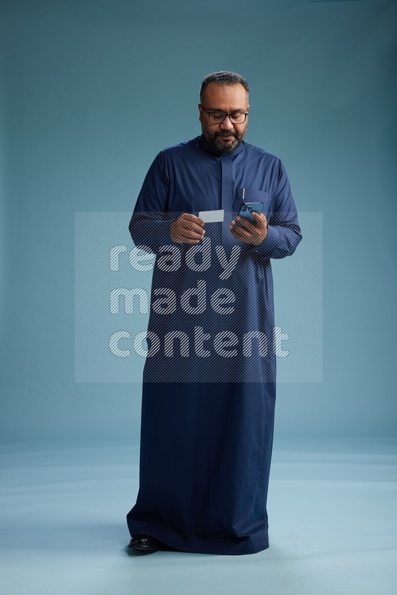 Saudi Man without shimag Standing holding ATM while talking on phone on blue background