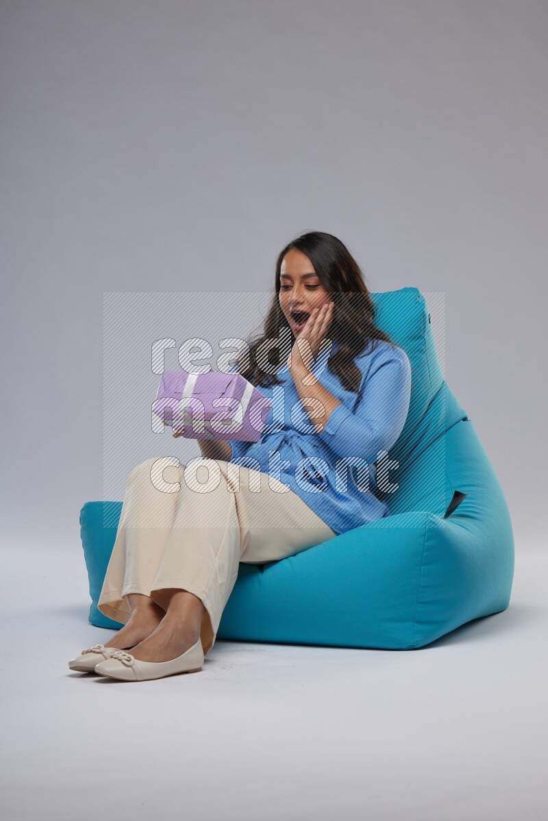 A woman sitting on a blue beanbag and holding a gift