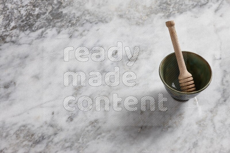 Decorative pottery bowl with wooden honey dipper in it on grey marble background