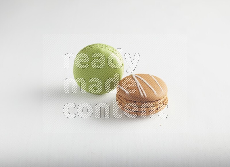 45º Shot of of two assorted Brown Irish Cream, and Green Pistachio macarons on white background