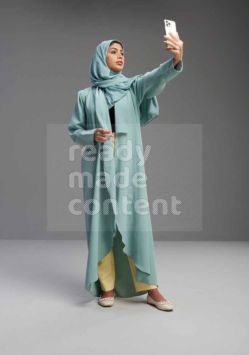 Saudi Woman wearing Abaya standing taking selfie on Gray background