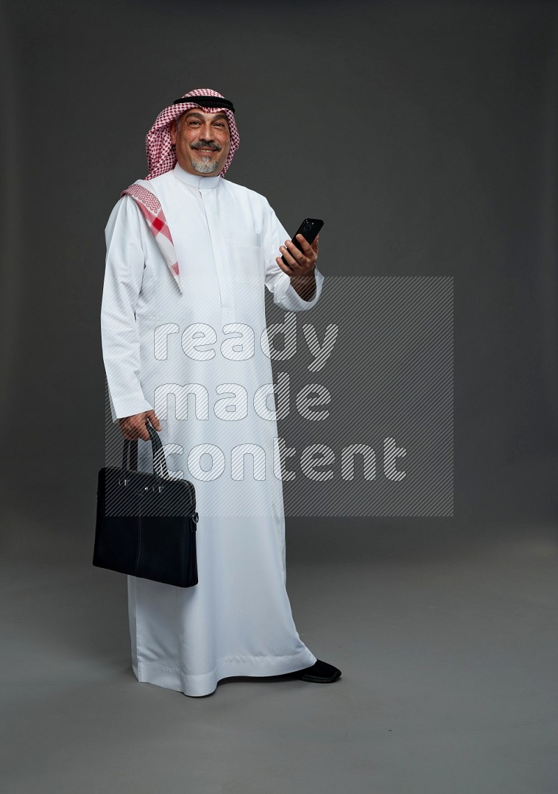 Saudi man with shomag Standing holding bag and phone on gray background