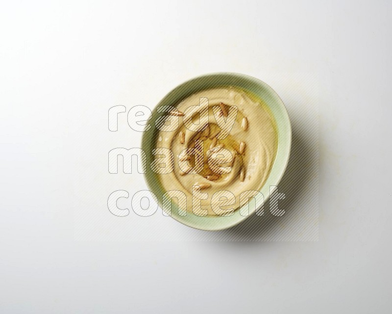 Hummus in a green plate garnished with pine nuts on a white background