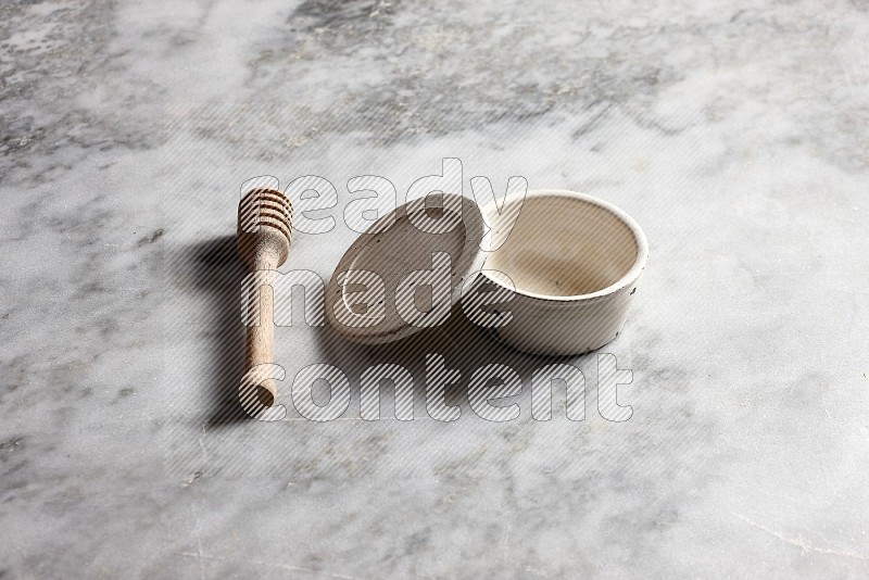 White Pottery Bowl with wooden honey handle on the side with grey marble flooring, 45 degree angle