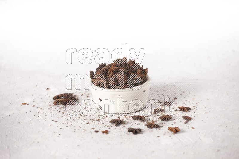 Star Anise in a white bowl and more of it sprinkled on white background