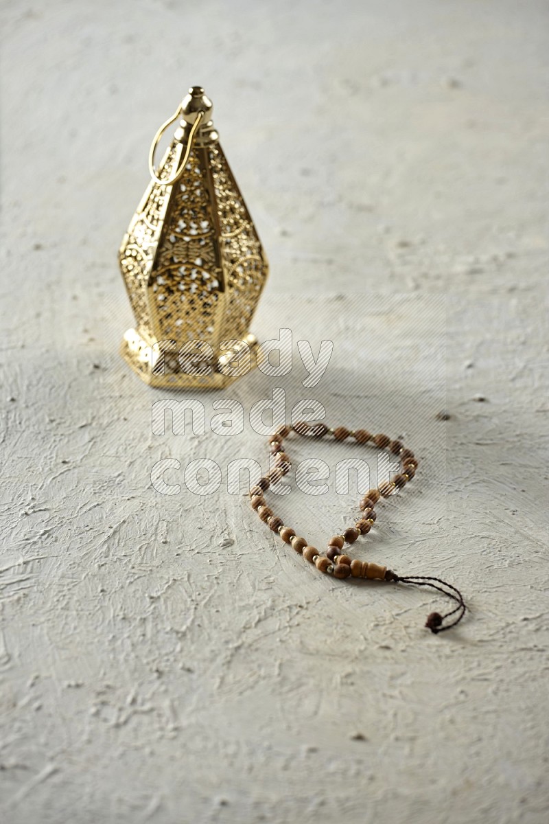 A golden lantern with different drinks, dates, nuts, prayer beads and quran on textured white background