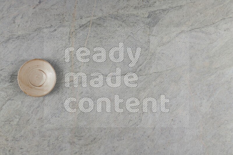 A circular beige pottery plate on grey marble background