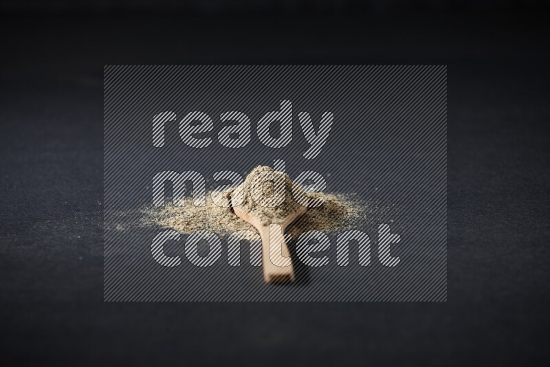 ملعقة خشبية ممتلئة ببودرة الهيل والبودرة تناثرت على خلفية سوداء