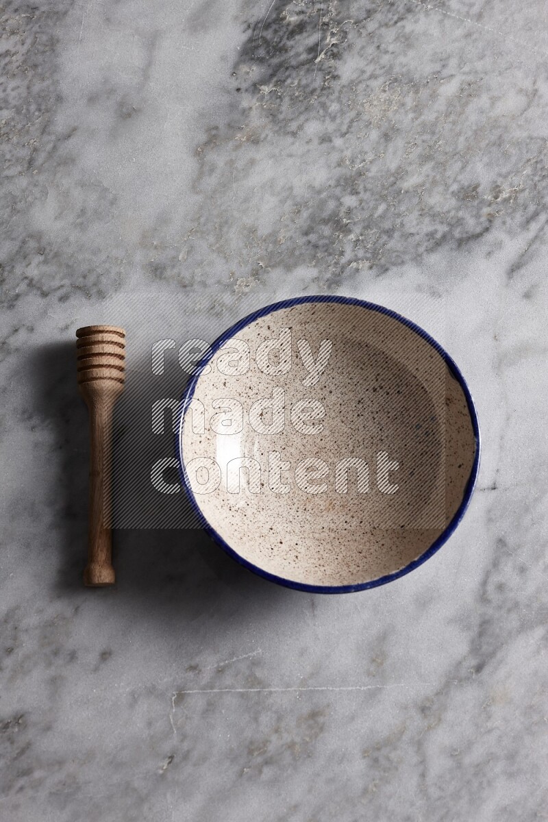 Multicolored pottery bowl with wooden honey dipper on the side on grey marble background