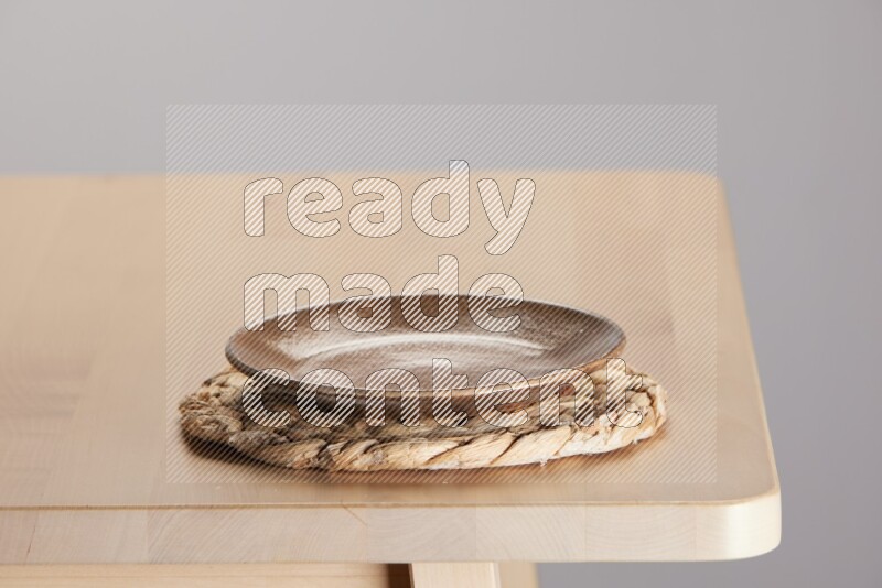 multi-colored pottery Plate placed on a small light colored straw placemat on the edge of wooden table