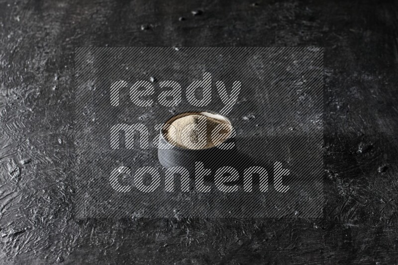 وعاء فخار أسود مملوء ببودرة الفلفل الأبيض على أرضية سوداء