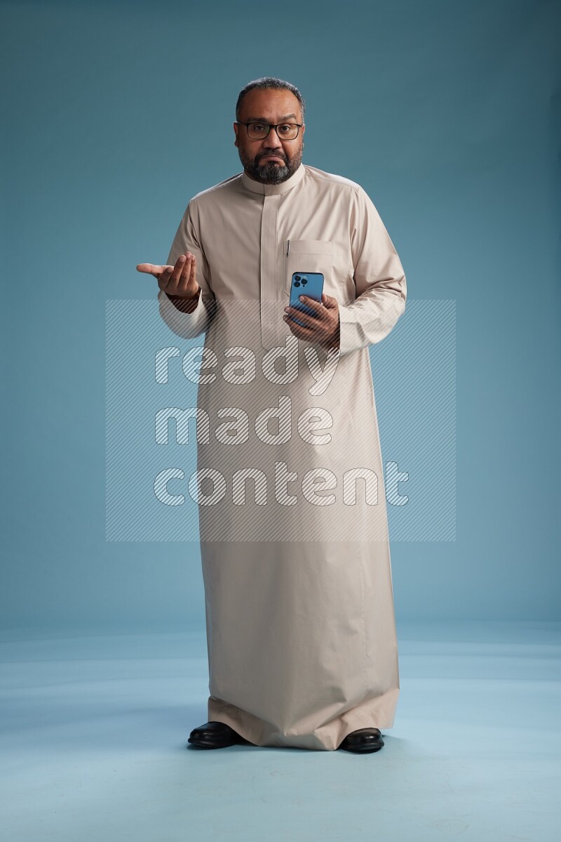 Saudi Man without shimag Standing texting on phone on blue background