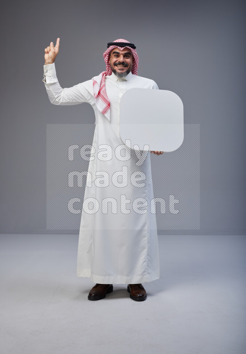 Saudi man Wearing Thob and red Shomag standing holding social media sign on Gray background
