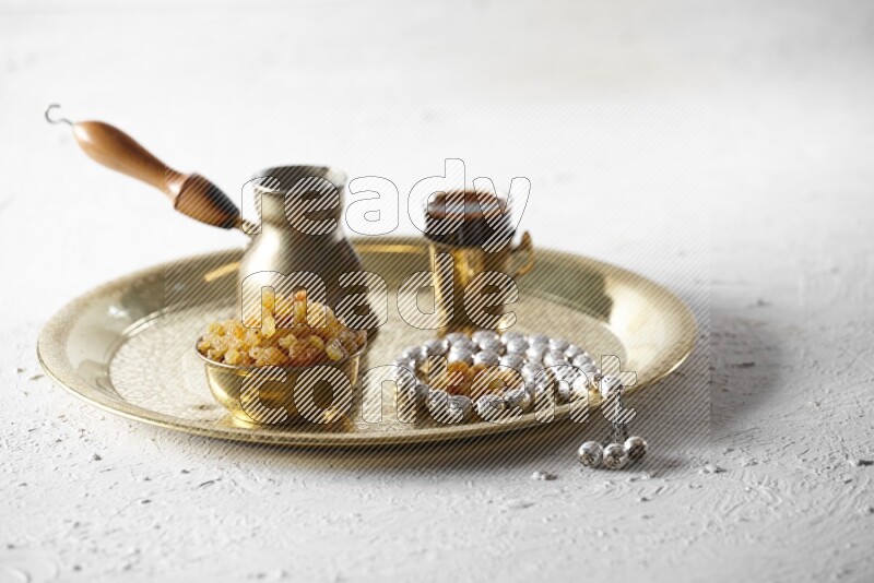 Raisins in a metal bowl with coffee and prayer beads on a tray in a light setup