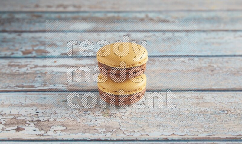45º Shot of two Yellow and Brown Chai Latte macarons on light blue wooden background