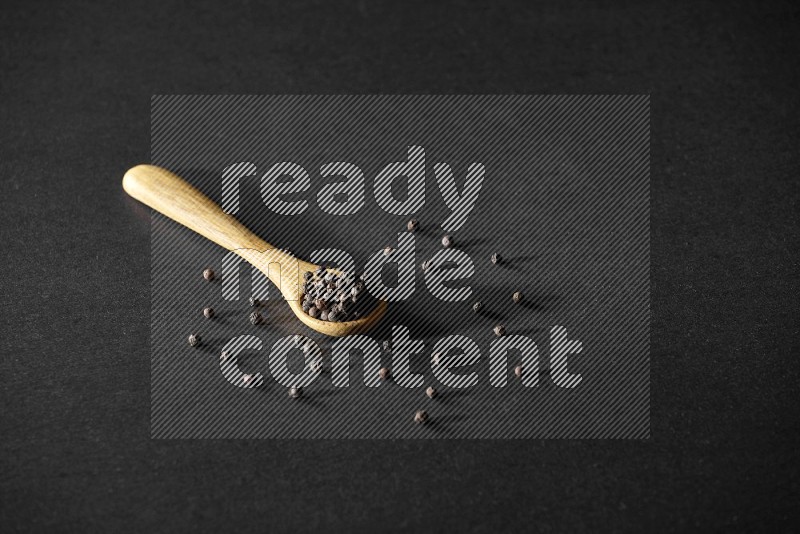 A wooden spoon full of black pepper on a black flooring