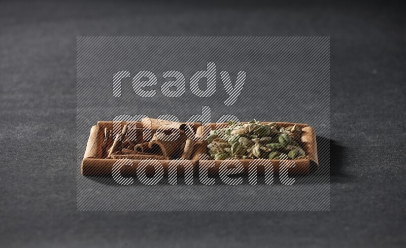 مربعان من أعواد القرفة ممتلئان بحبوب الهيل والقرفة علي خلفية سوداء