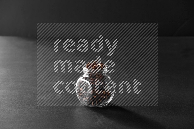 A glass spice jar full of star anise on black flooring