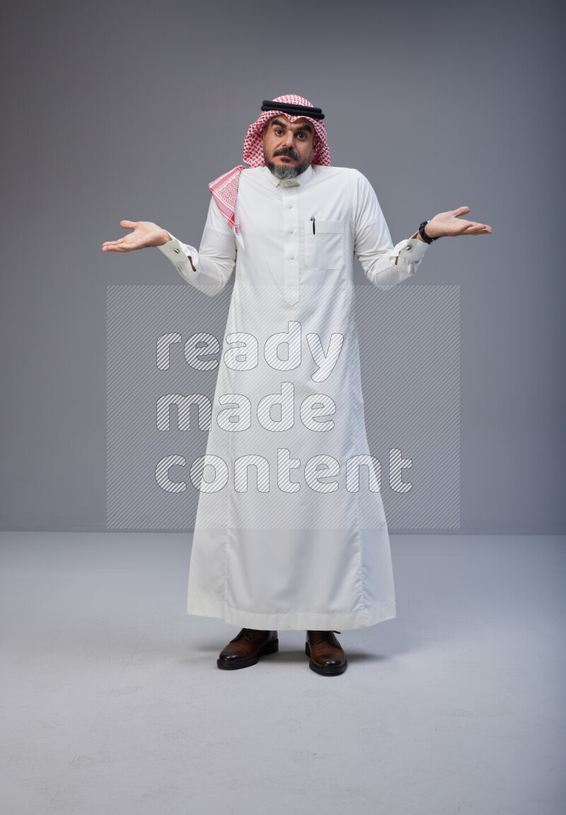 Saudi man Wearing Thob and red white Shomag standing interacting with the camera on Gray background