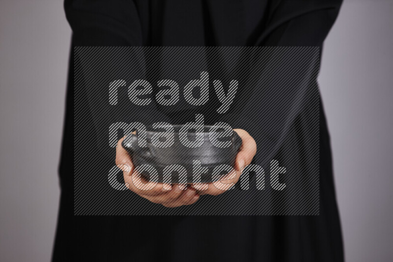A woman in black abaya holding different pottery essentials in different positions