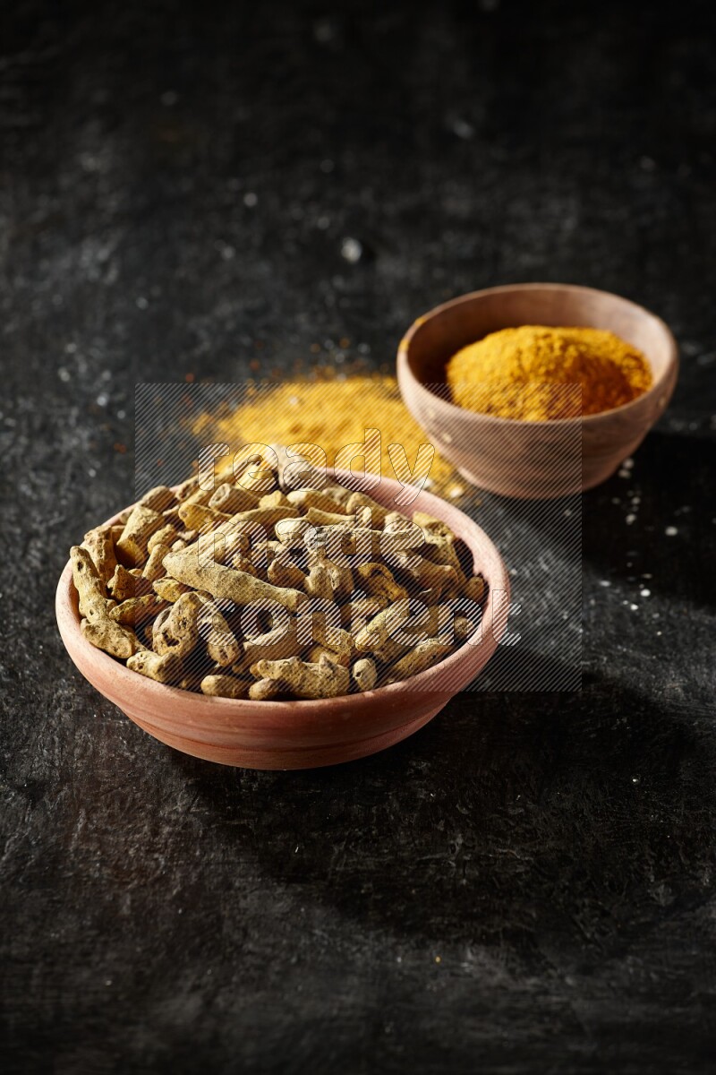 وعاءان خشبيان، أحدهما ممتلئ ببودرة الكركم والآخر بأصابع الكركم المجففة، على خلفية سوداء