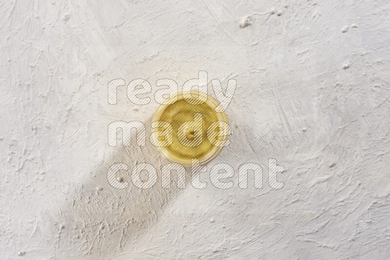 A glass jar full of mustard paste on a textured white flooring