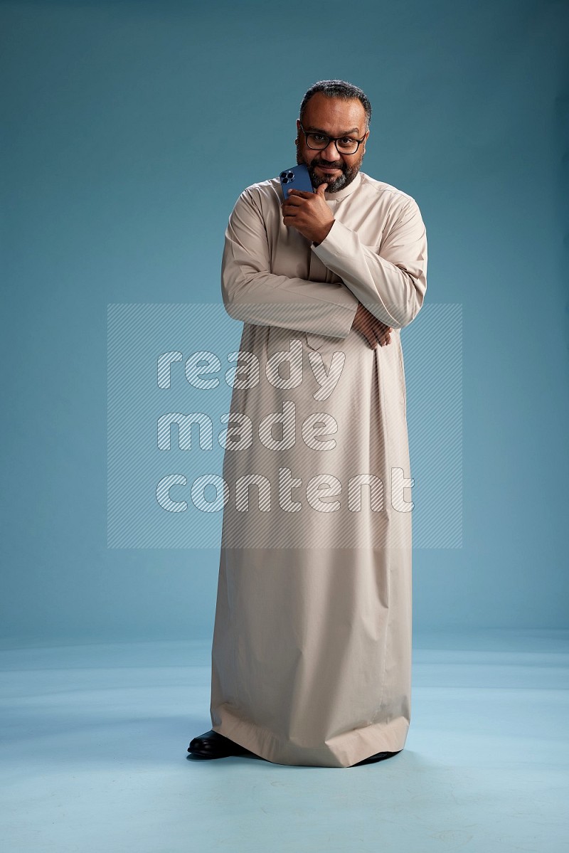 Saudi Man without shimag Standing texting on phone on blue background