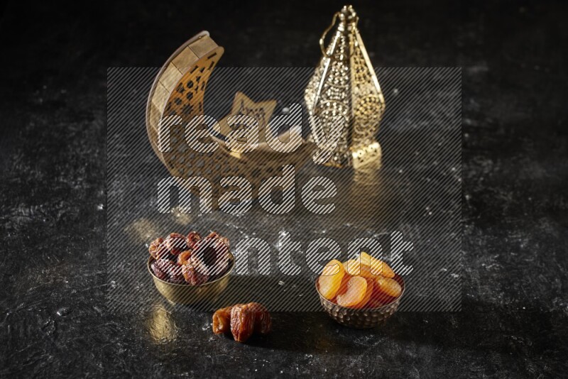 Dates in a metal bowl with dried apricot beside golden lanterns in a dark setup