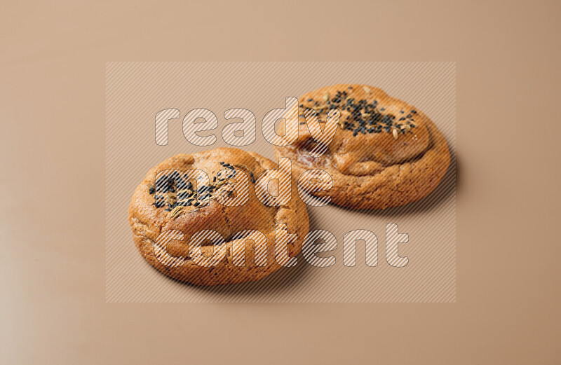 Two chocolate chip cookies on a brown background