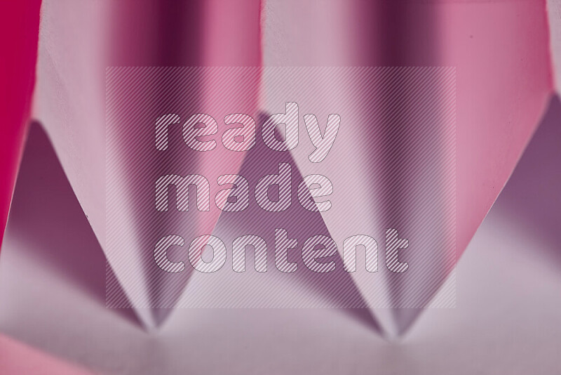 صورة مجردة مقربة تظهر طيات ورقية هندسية حادة بتدرجات اللون الوردي