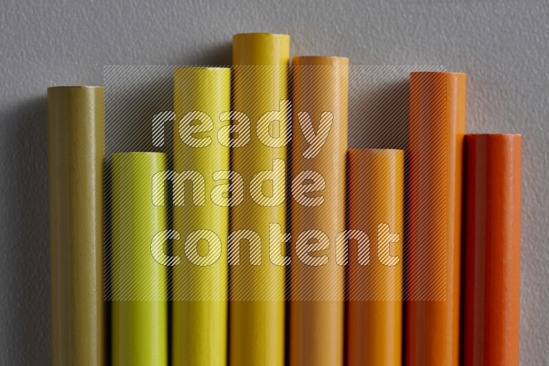 A collection of sharpened colored pencils arranged showcasing a gradient of yellow and orange hues on grey background