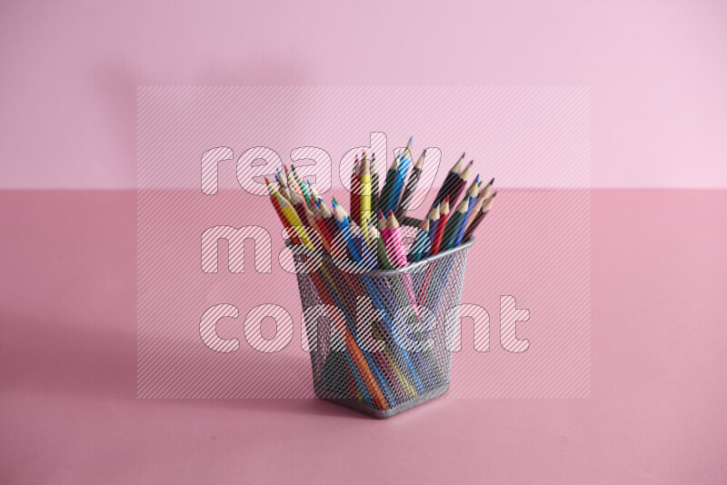 Pens, pencils and other different school supplies in a metal pen holder on rose background
