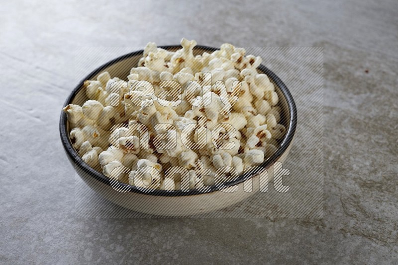 popcorn in a multi-colored pottery bowl on a grey textured countertop