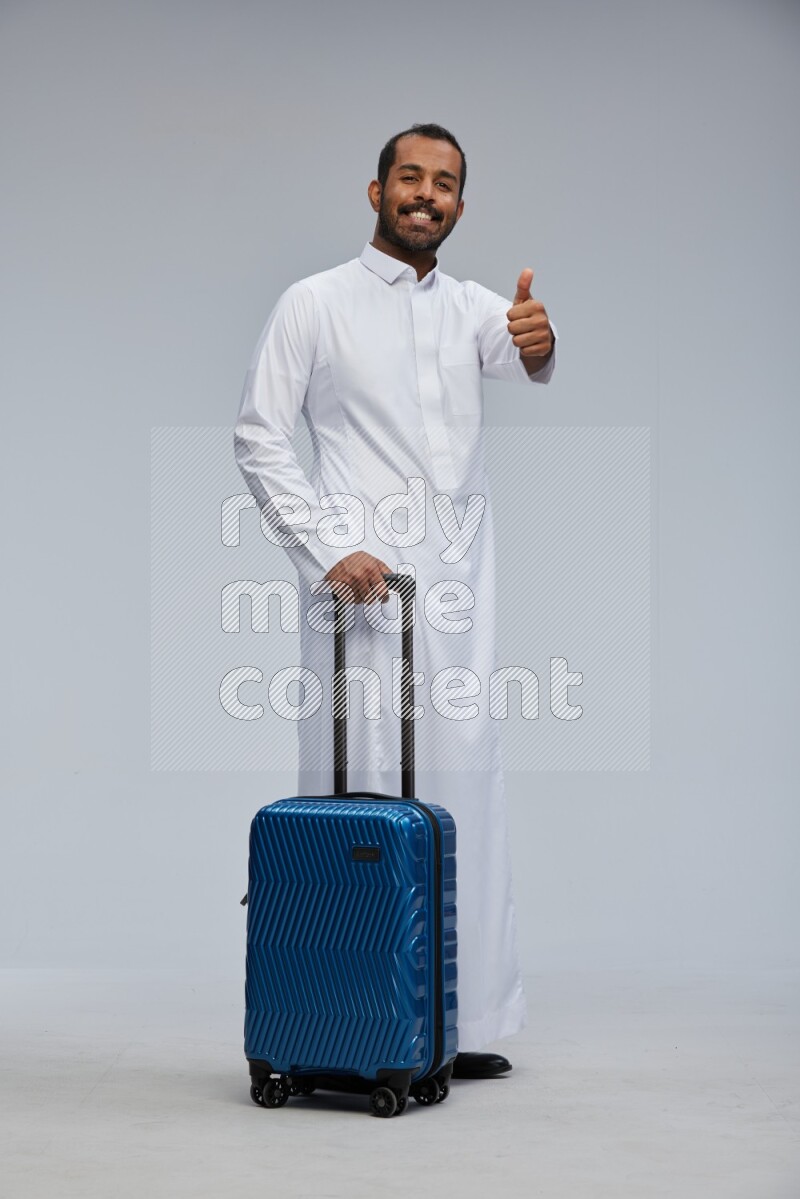 Saudi man wearing thob standing holding Travel bag on Gray background