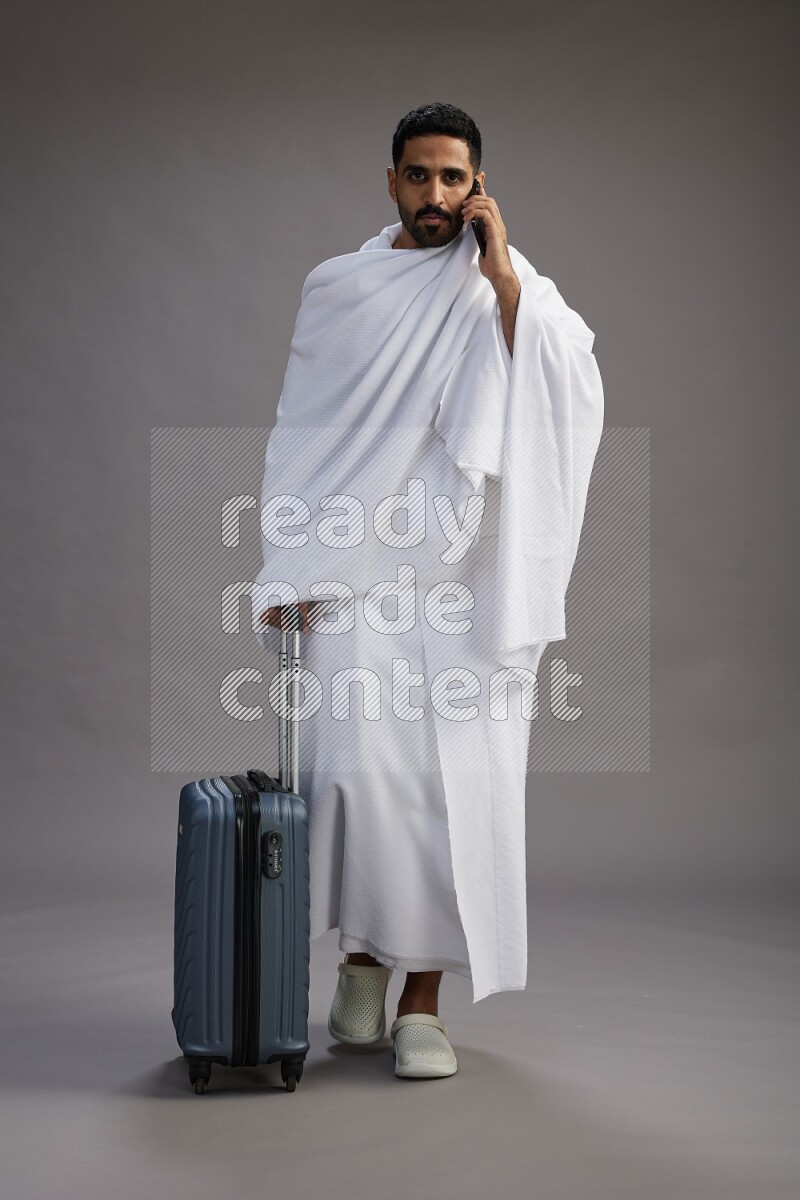 A man wearing Ehram Standing holding traveling bag on gray background