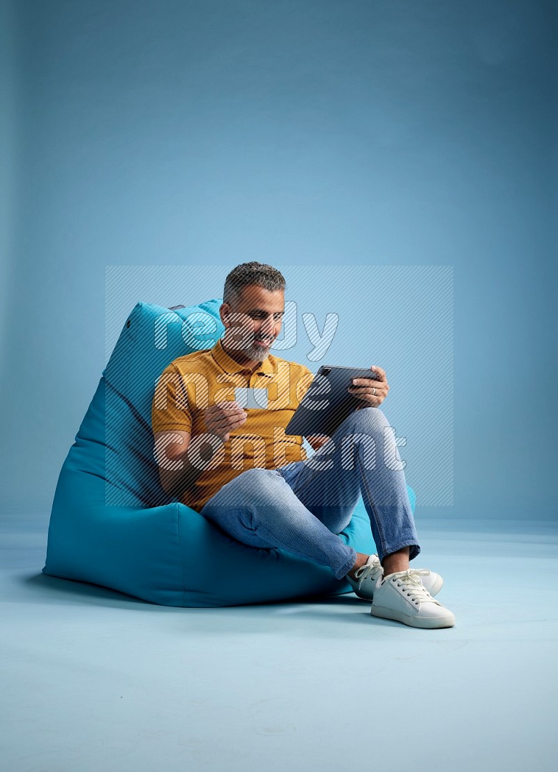 A man sitting on a blue beanbag and holding ATM card with tablet