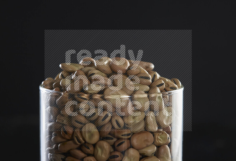 Fava beans in a glass jar on black background