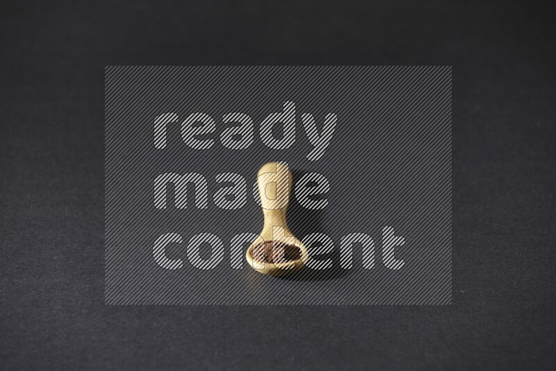 A wooden spoon full of cloves powder on a black flooring