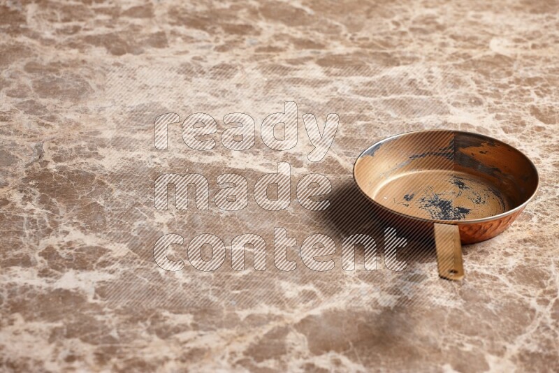 A small copper pan on beige marble background