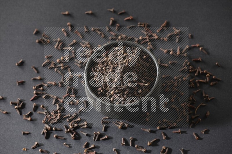 A black pottery bowl full of cloves on a black flooring