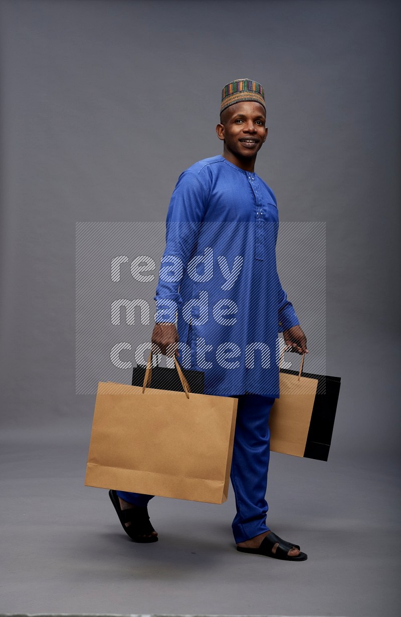 Man wearing Nigerian outfit standing holding shopping bag on gray background