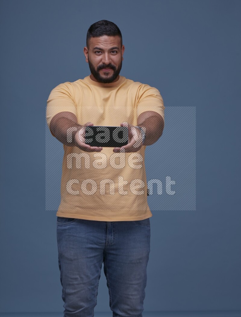 رجل يرتدي بنطال ازرق جينز وقميص اصفر بأكمام قصيره يشير الى جواله