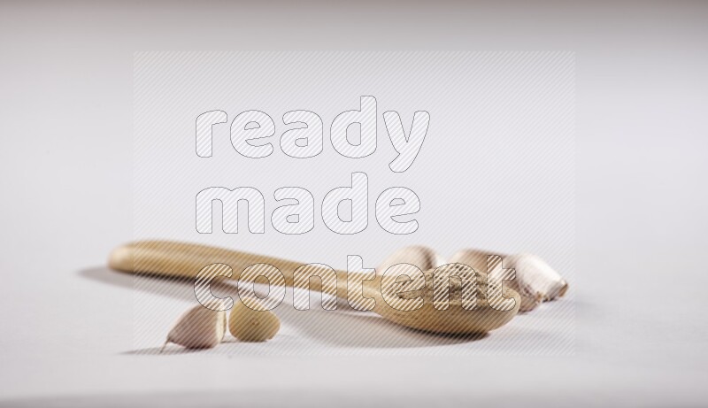 A wooden spoon full of garlic powder with cloves beside it on a white flooring
