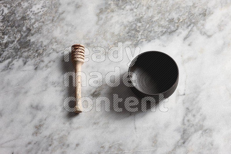 Black Pottery bowl with wooden honey handle on the side with grey marble flooring, 65 degree angle