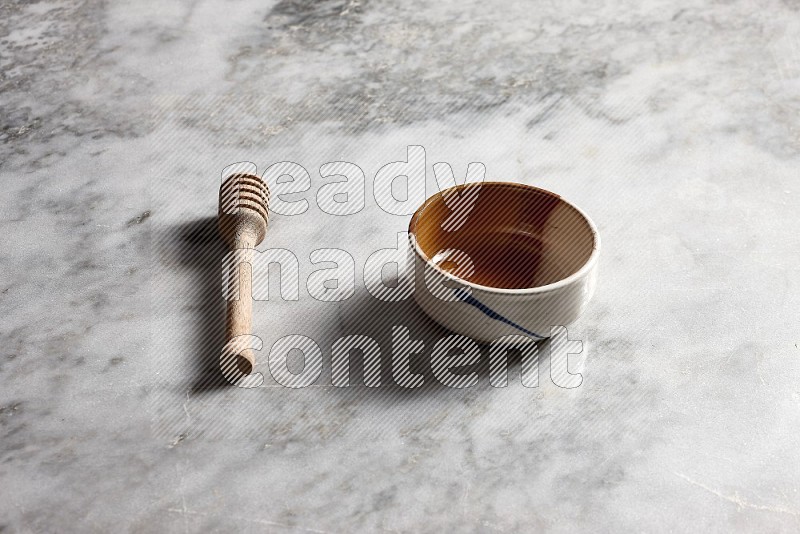 Multicolored Pottery bowl with wooden honey handle on the side with grey marble flooring, 45 degree angle